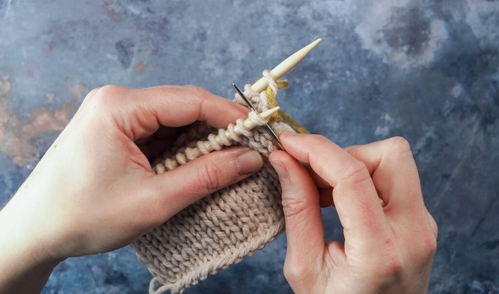 Hands hold knitting needles with threads and a needle for sewing